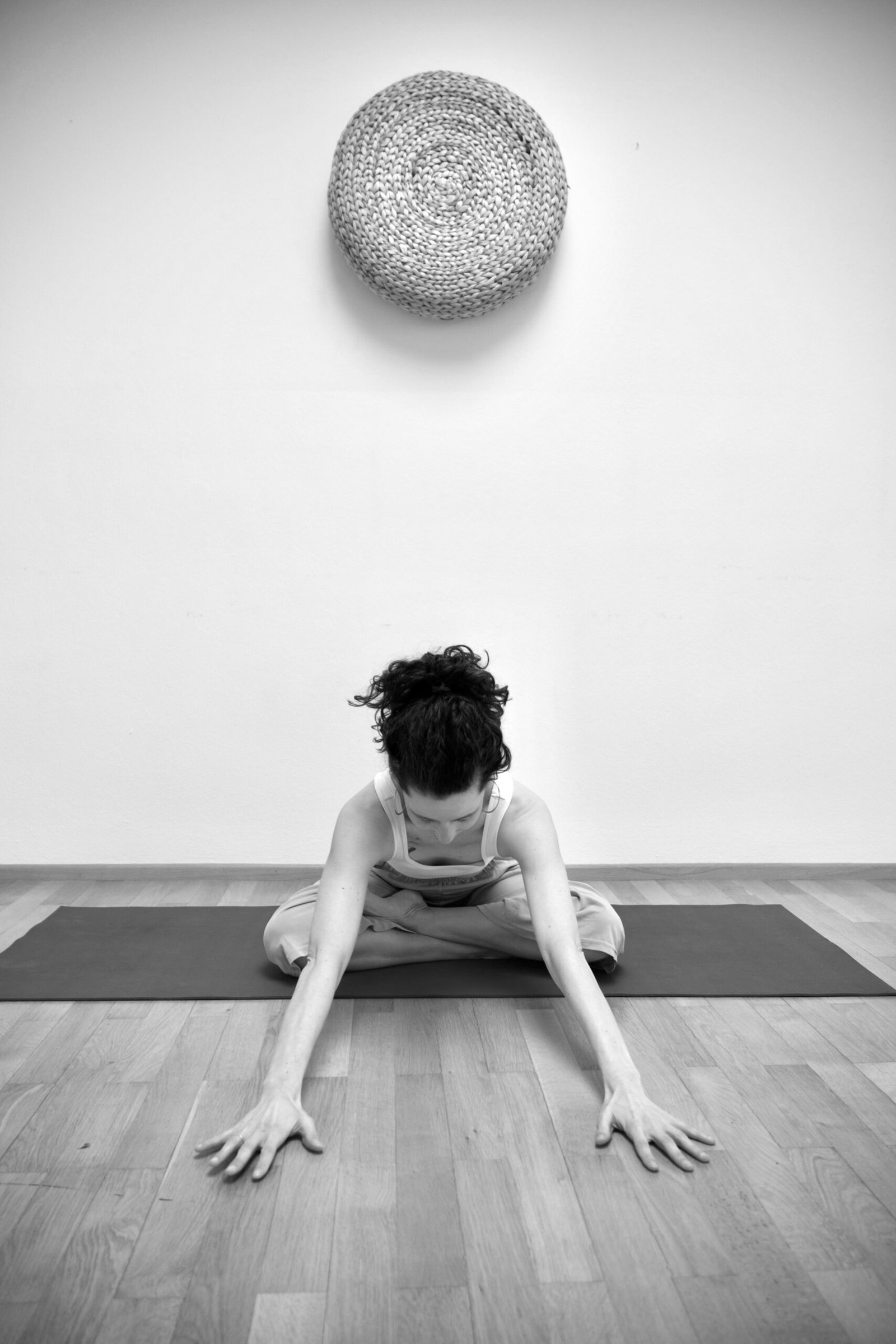 schwarz-weiß foto von Frau auf Yogamatte in vorgelehnter Yogapose Lotussitz mit Blick auf den Boden